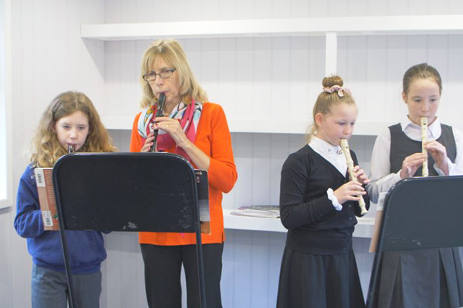 Children with teacher playing the recorder inside an room with white walls